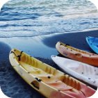 Picture of four kayaks (two orange, one white, and one blue) laying on a beach near the water